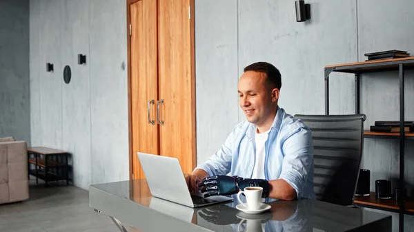 Smiling man programmer with artificial bio hand prothesis types on laptop keyboard — Stock Photo, Image