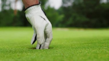 Beyaz eldivenli erkek eller delikten bir golf topu alır.