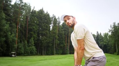 Genç adam sahada golf oynuyor.