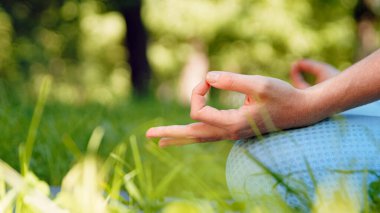 Mavi eşofmanlı genç kadın spor eğitmeni yoga pozisyonunda meditasyon yapıyor. Elleri yeşil çayırda.