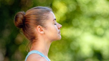 Sarışın kadın, yoga pozisyonunda oturmuş yeşil çayır çimlerine poz veriyor.