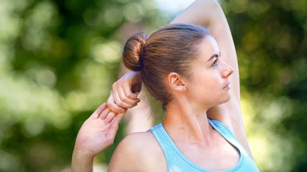 Mujer atleta profesional con moño de pelo claro en top azul estira las manos y la espalda —  Fotos de Stock