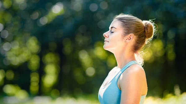 Young woman athlete with hair bun relaxes after exercises and meditates standing in yoga pose — Stock Photo, Image