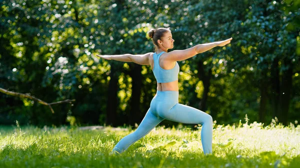 Young woman yoga trainer stands in static asana on green meadow grass — Stock Photo, Image
