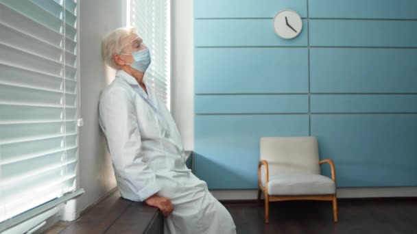 Trött läkare tar av masken sitter på fönsterbrädan på kliniken — Stockvideo