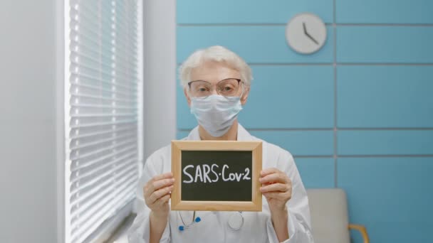 Kıdemli doktor elinde SARS Cov 2 yazılı bir karatahta tutuyor. — Stok video