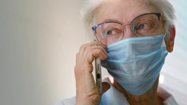 Kvinna läkare i mask talar på mobiltelefon vid ljus vägg — Stockvideo