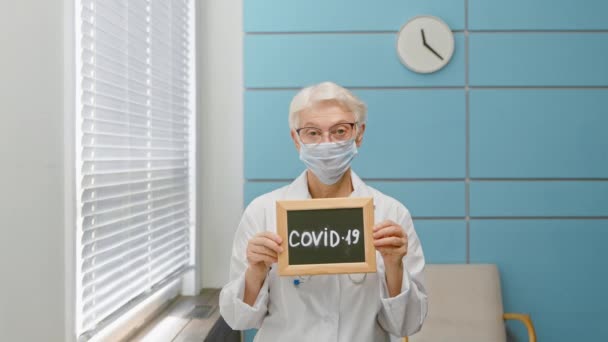 Médico senior sostiene pizarra con palabra Covid 19 en la oficina — Vídeos de Stock