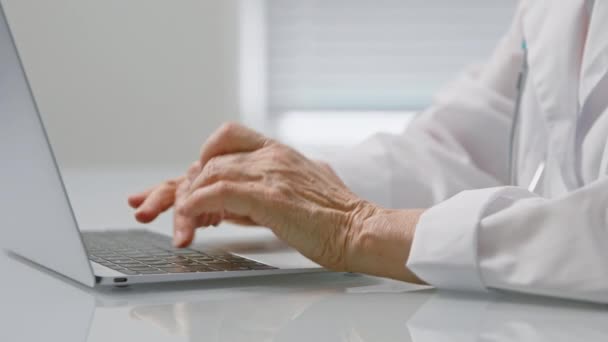 Gammal medicinsk arbetare skriver text på laptop sitter vid bordet — Stockvideo