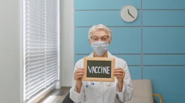 Maskeli doktor klinikte kelime aşısıyla karatahta tutuyor.
