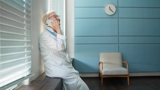Šťastný doktor s brýlemi rozhovory na mobilu v nemocnici — Stock video