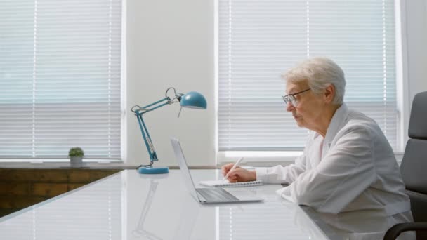 Doctor escribe hablando con el paciente en videochat en la clínica — Vídeos de Stock