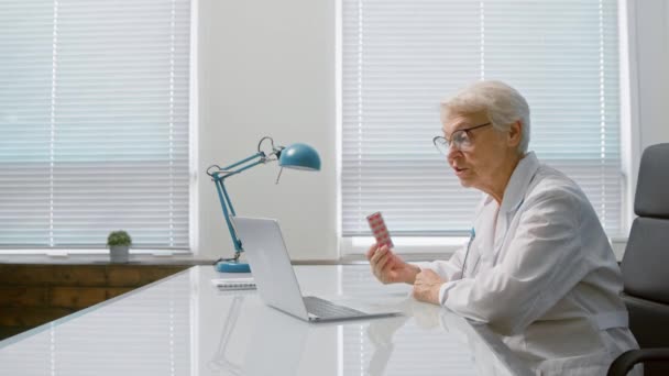 Dokter toont pillen op videocall via laptop in kliniek — Stockvideo