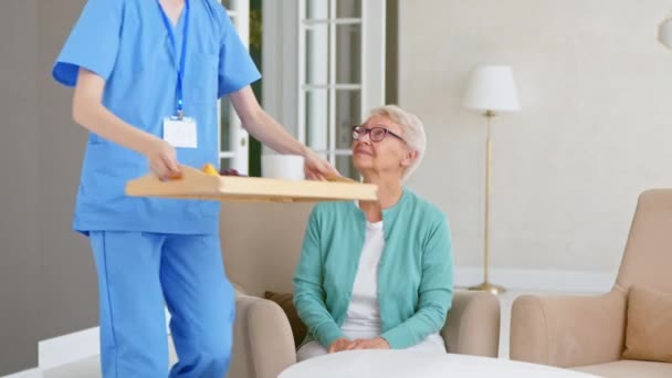 Pflegerin trägt Tablett bei sich und stellt Essen für alten Patienten auf den Tisch — Stockvideo