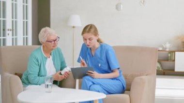 Yaşlı kadın elinde haplarla sarışın doktorun tavsiyelerini dinliyor.