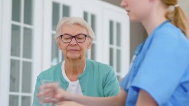 Tıp çalışanı odasındaki olgun kadına bir bardak su verir.