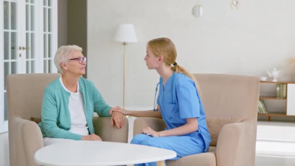 Bionda medico parla tirando su la donna anziana in ufficio luce — Video Stock