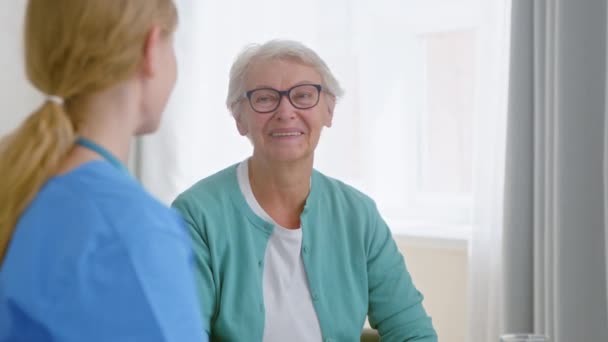 Verpleegster praat met senior vrouw patiënt en geeft water in de afdeling — Stockvideo