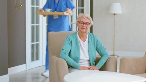 Caretaker draagt ontbijt naar volwassen dame in verpleeghuis — Stockvideo