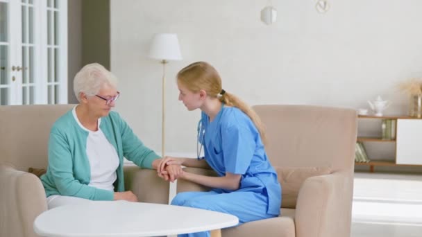 Pozytywny lekarz łączy ręce rozweselając starszą panią w klinice — Wideo stockowe
