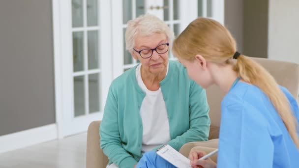 Dokter interviewt oude dame patiënt maakt aantekeningen in het kantoor — Stockvideo