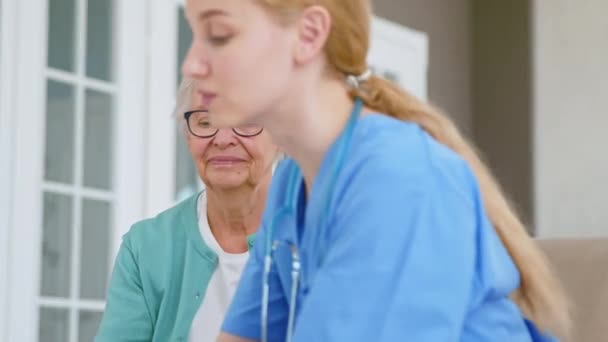 Обережна медсестра дає чашку старшій пацієнтці в кімнаті — стокове відео