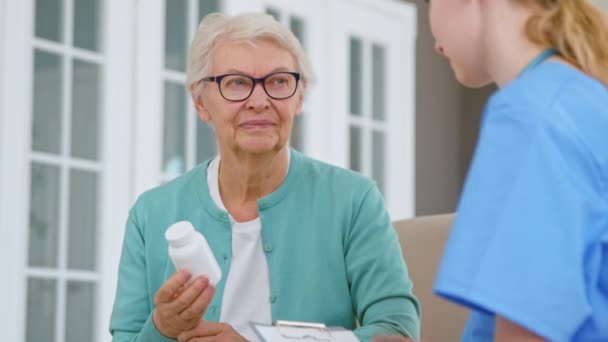 Vieja mujer sostiene pastillas botella escuchar al médico en la habitación — Vídeo de stock