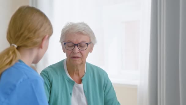 Senior dame met bril praat met jonge conciërge door raam — Stockvideo