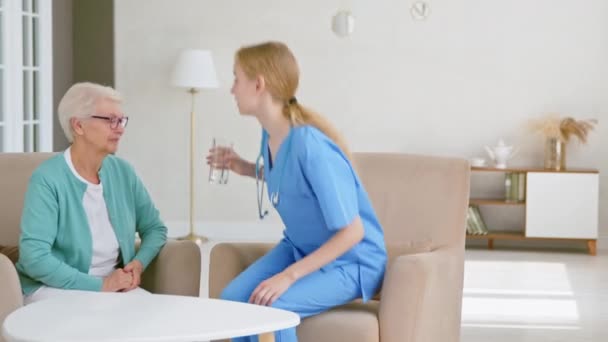 Medische werker draagt water naar volwassen dame zitten aan tafel — Stockvideo