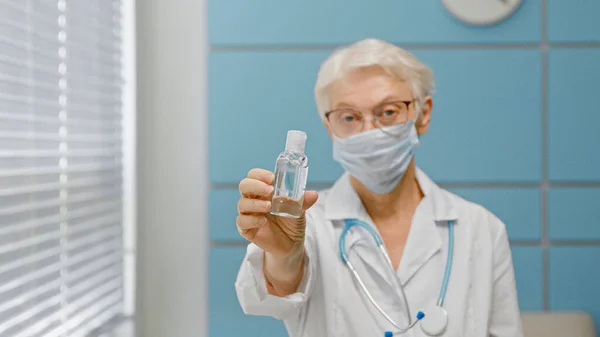 Skilled female doctor with glasses and protective mask stands in light hospital office focus on hand — Stock Photo, Image