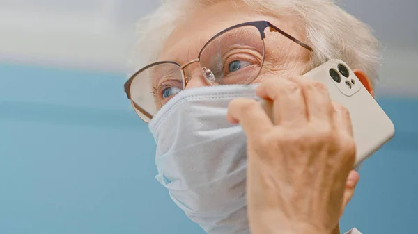 Positivo anziano signora medico in maschera monouso colloqui sul paziente di consulenza cellulare in ufficio ospedaliero — Foto Stock