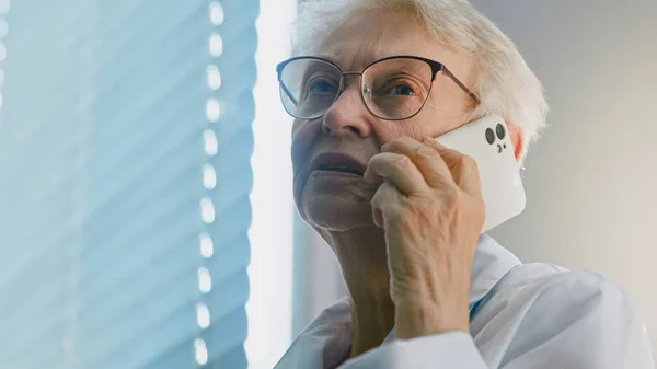 휴대 전화로 안경을 쓰고 있는 성숙 한 여의사 가 병원에 있는 환자들에게 추천 연설을 한다 — 스톡 사진