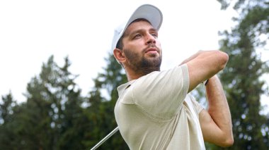 Şapkalı genç adam yakın planda golf oynuyor.