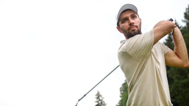 Şapkalı genç adam yakın planda golf oynuyor.