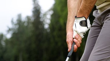 Sahada golf sopası tutan bir oyuncunun elleri.