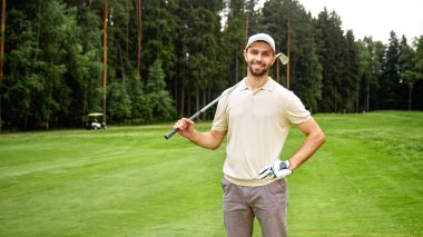 Golf sopalı genç adam golf sahasında kameraya bakıyor.
