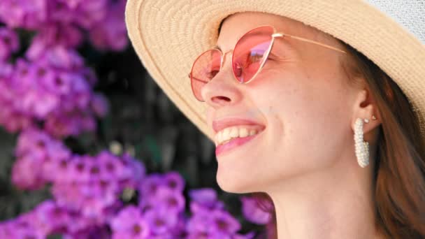 Muchacha sonriente en un sombrero en flores lila — Vídeos de Stock