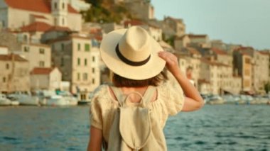 Şapkalı genç gezgin rıhtımdan denize bakıyor, yavaş çekim video 6k