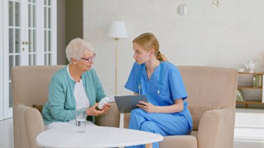 Dosyası olan genç bayan doktor, ışık ofisteki yaşlı gri saçlı kadın hastayla yapılan testlerin sonuçlarını anlatıyor.