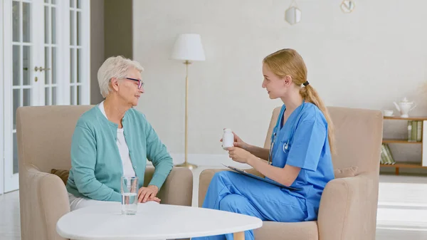 Ärztin zeigt Seniorin, die im Büro in Sesseln sitzt, Flasche mit Medikamenten — Stockfoto