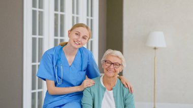 Steteskoplu güzel genç doktor kameraya poz veren gülümseyen yaşlı kadın hasta.