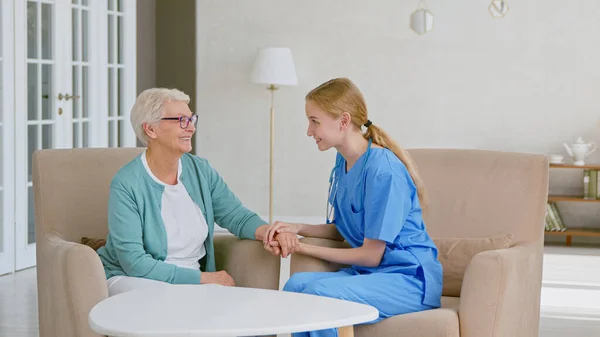 Médecin positif joint les mains pour réconforter femme aux cheveux gris mature assis dans des fauteuils dans un bureau élégant — Photo