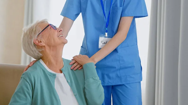 Caretaker hugs smiling mature grey haired lady in spacious room — Stock Photo, Image