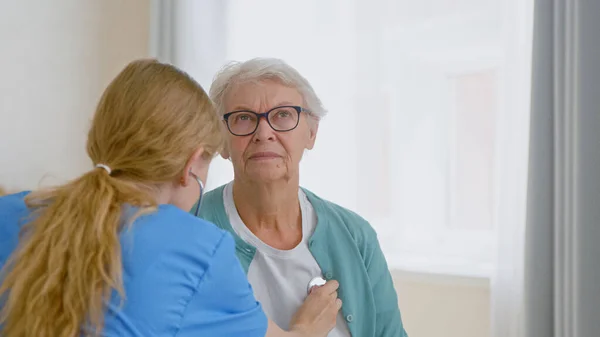 Seniorin unterzieht sich Untersuchung mit Stethoskop und Arzt hört Herzschlag Stockbild