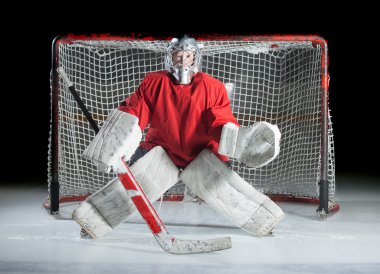 A young ice-hockey goaltender in a ready position against a dark clipart