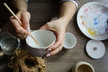 Seramik el yapımı bir kaseyi elle boyama işlemi. Sanatçının güzel kadın ellerine dikkat edin..
