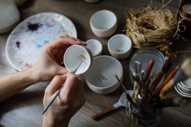 Seramik el yapımı bir kaseyi elle boyama işlemi. Sanatçının güzel kadın ellerine dikkat edin..