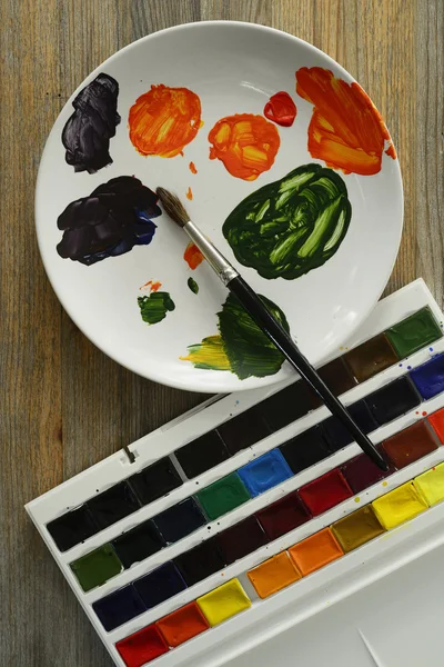 Кисть и краски на тарелке, деревянный фон — стоковое фото