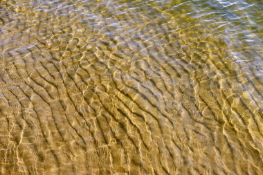 Suyun yüzeyi güneş ışınları tarafından delinir, kumlu tabanı su yoluyla görülebilir.