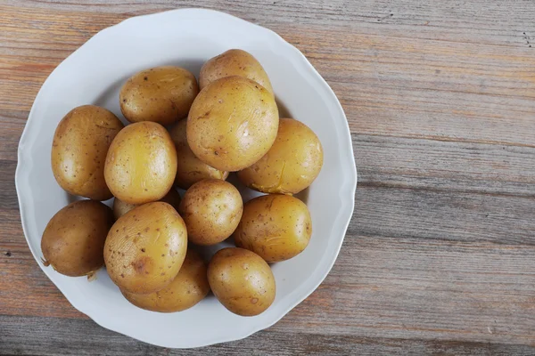 Gekookte aardappelen in hun huid op een plaat, houten achtergrond — Stockfoto